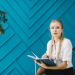 portrait-happy-therapist-with-notes-sitting-against-blue-design-wall-1024x683